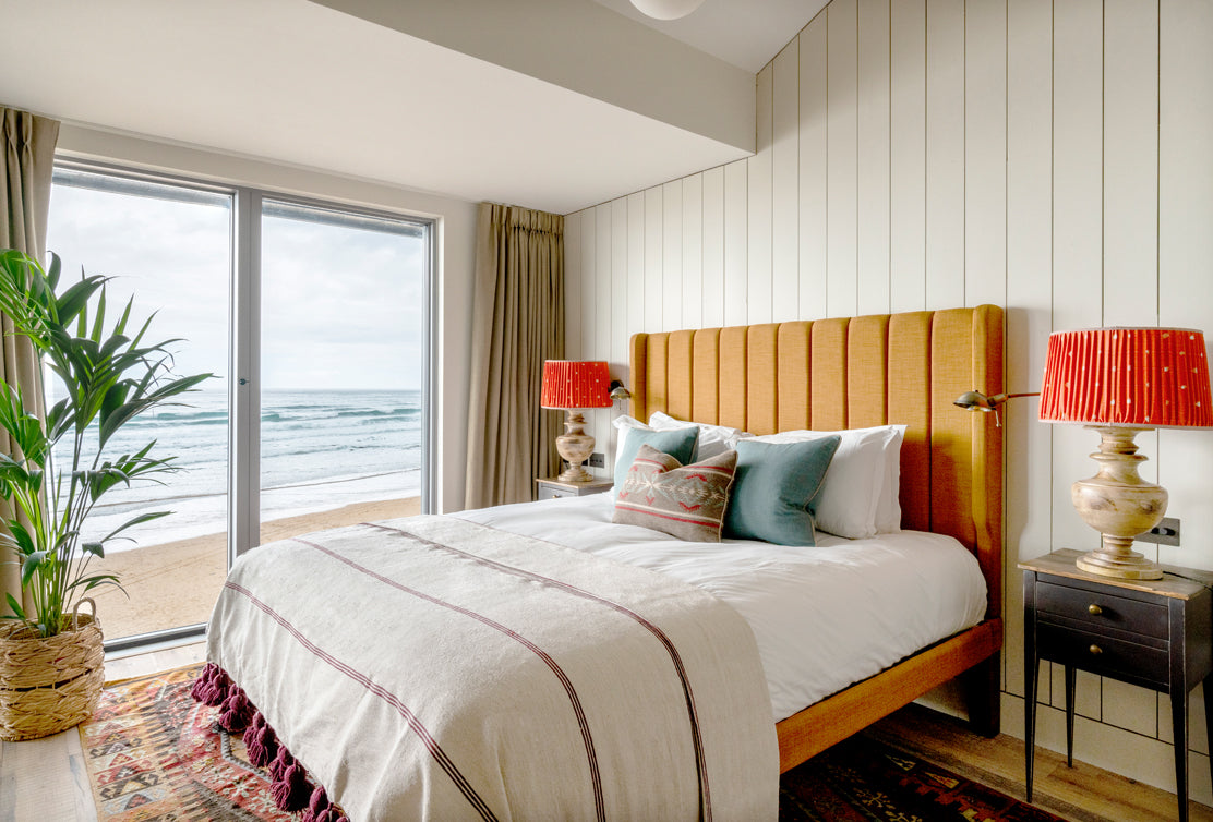 Cozy bedroom with a beach view featuring a large orange headboard, decorative pillows, and vibrant lamps next to a window.