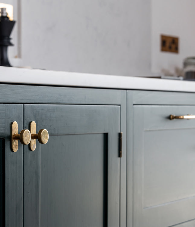 Close-up of modern cabinetry featuring dark green paint, natural wood accents, and a circular brass knob for a sleek, contemporary look.