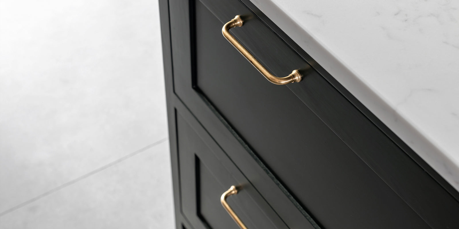 Close-up of black kitchen cabinet drawers featuring elegant gold handles, set against a light marble countertop.