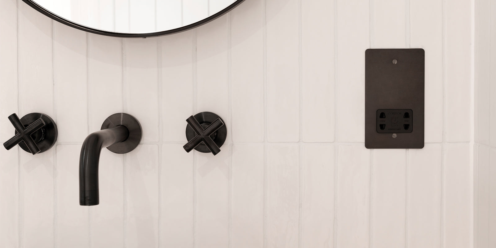 Close-up of a black faucet and wall-mounted controls against a white tiled wall, with a sleek black electrical outlet nearby.