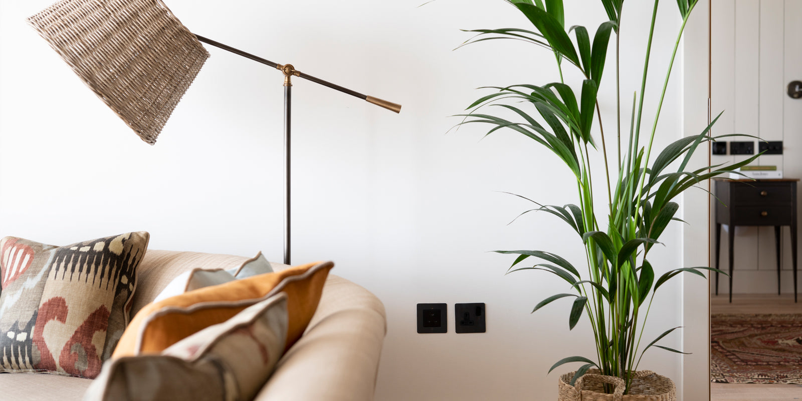 A cozy living space featuring a stylish floor lamp, colorful cushions on a sofa, and a tall green plant in a woven basket.