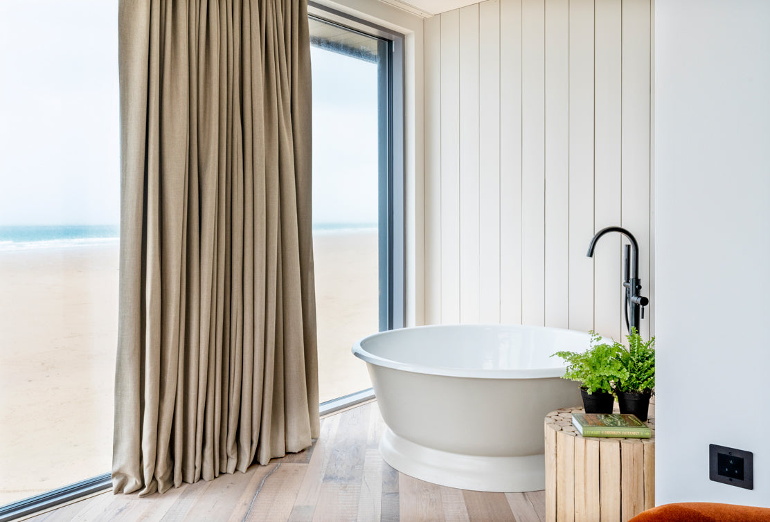 A minimalist wooden dresser with rounded edges, topped with a black lamp and a small diffuser, against a white shiplap wall.