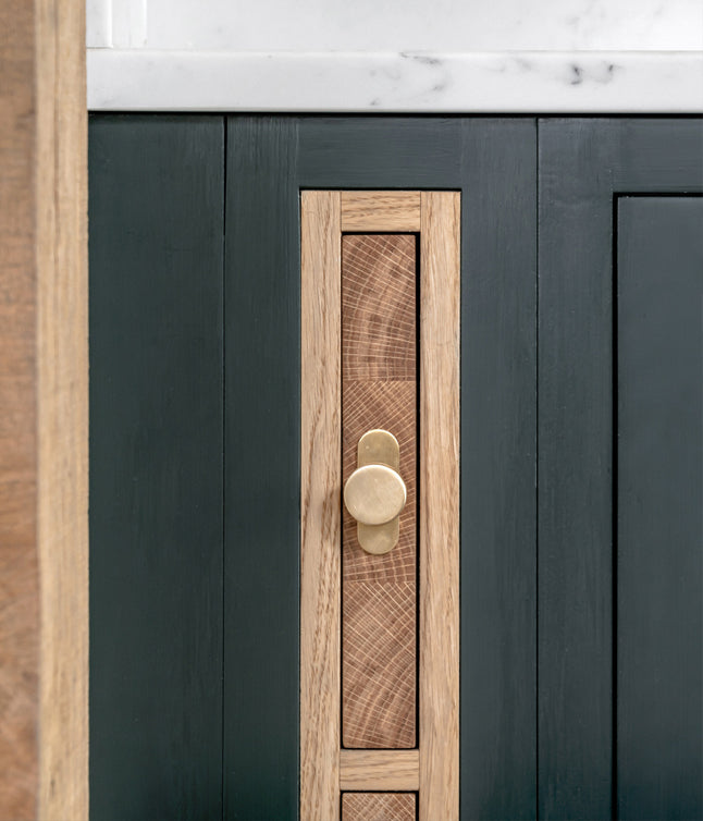 Close-up of modern cabinetry featuring dark green paint, natural wood accents, and a circular brass knob for a sleek, contemporary look.