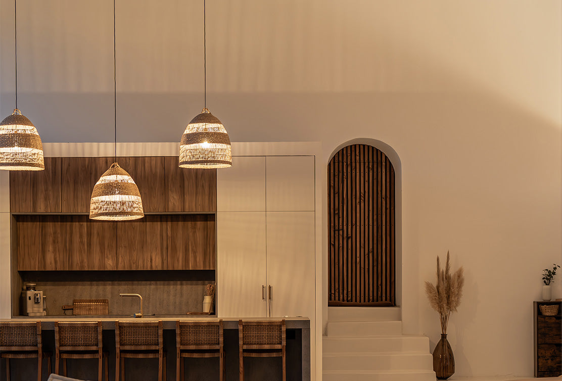 Modern kitchen with woven pendant lights, wooden cabinetry, and a staircase with a wooden arched entrance to the right.