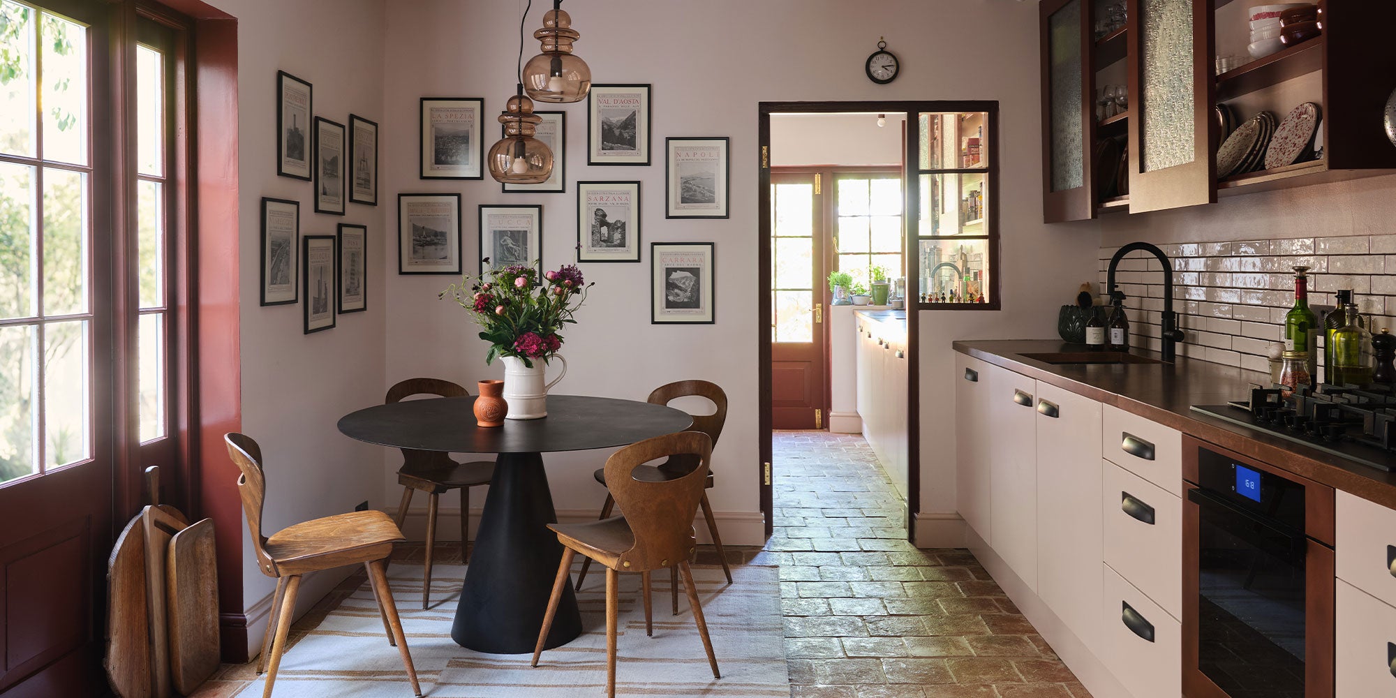A stylish kitchen featuring a round black table, wooden chairs, floral arrangement, and framed art on the walls, with a cozy entrance.