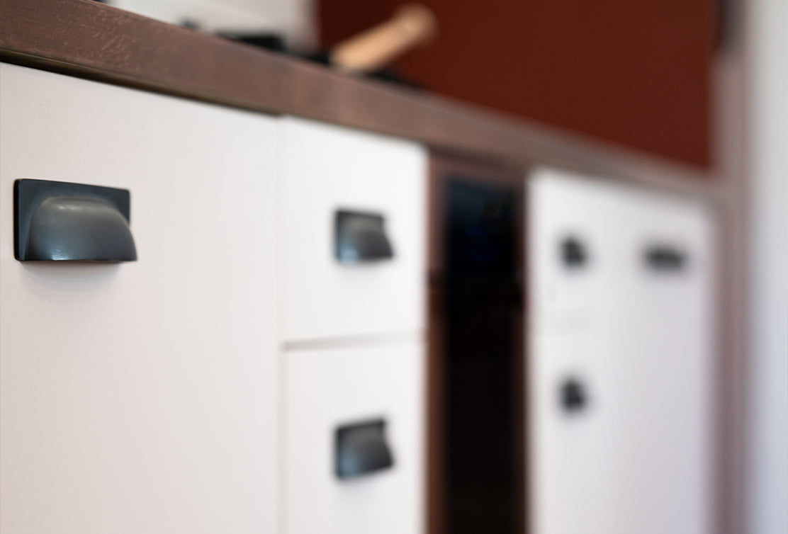 Close-up of white kitchen cabinets with black handles, wooden countertop, and a blurred background.