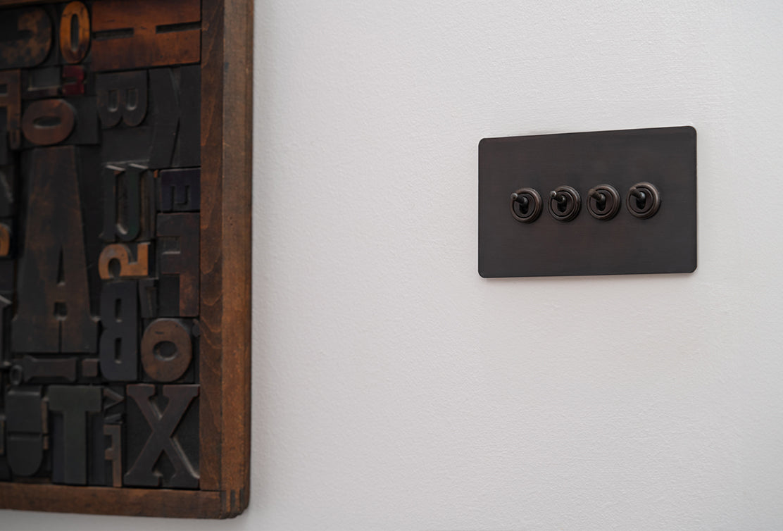 A modern light switch with four circular controls, mounted on a white wall beside a wooden frame filled with mixed typography.