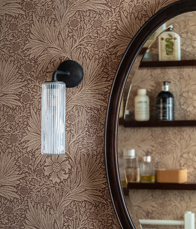 A stylish bathroom featuring floral wallpaper, a round mirror, a glass light fixture, and a minimalist sink with shelving.
