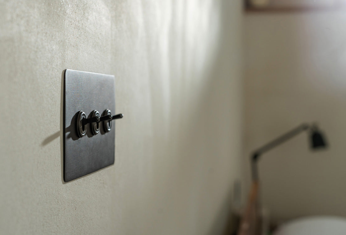 Close-up of a sleek black light switch on a textured wall, with soft natural light creating subtle shadows.
