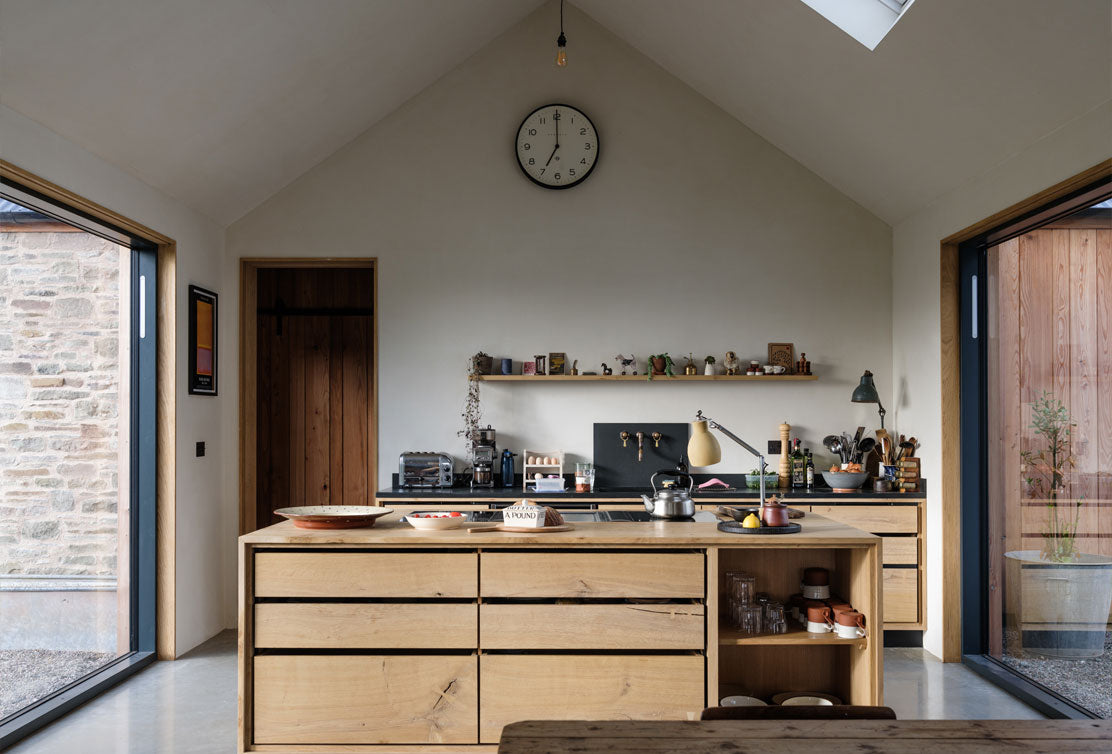 Modern kitchen with wooden cabinets, open shelving, and large windows, featuring minimalistic decor and natural lighting.