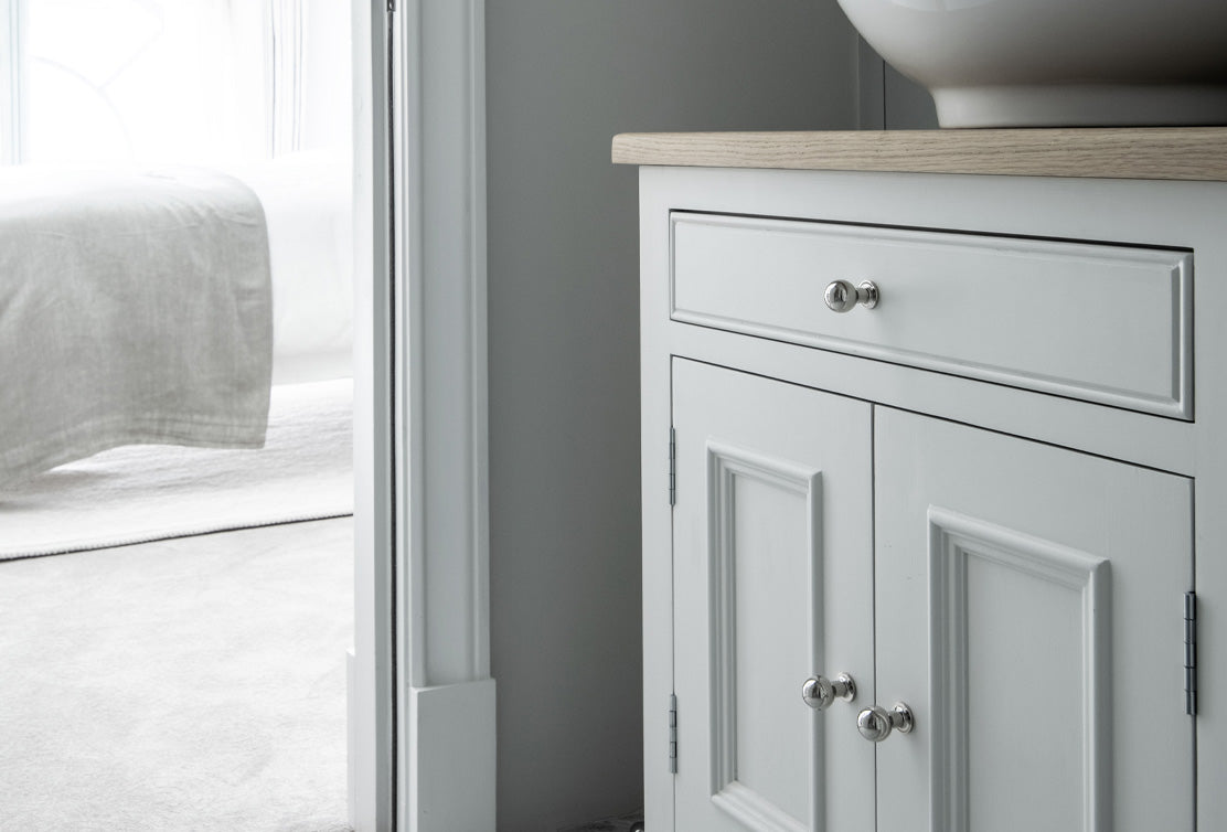 A corner of a stylish bathroom featuring a white cabinet with decorative paneling and a light wooden countertop.