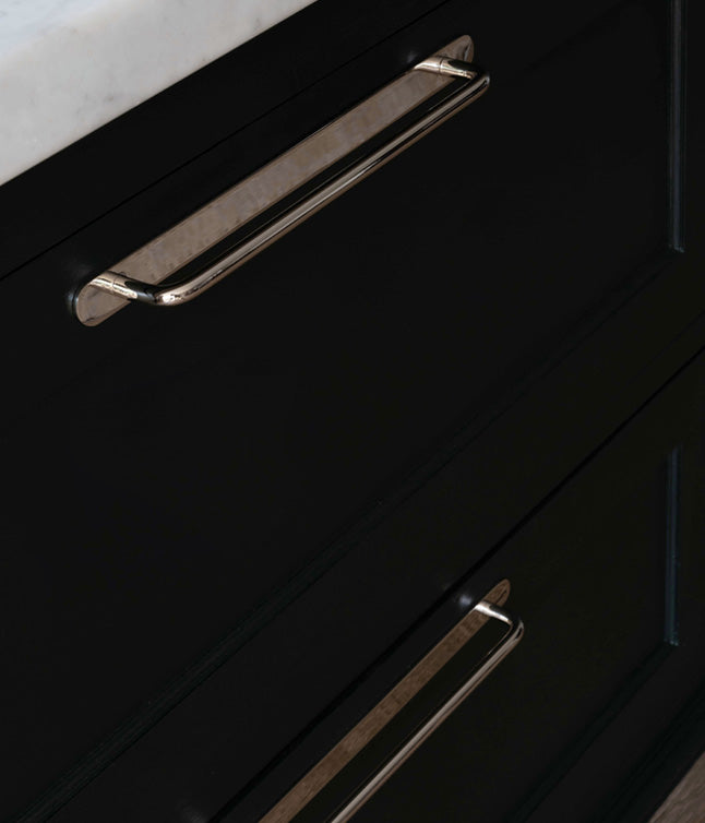 A close-up view of sleek silver drawer handles against a matte black cabinet with a marble countertop above.