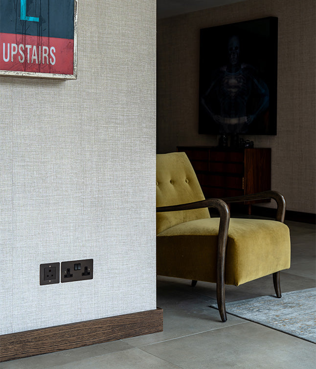 A cozy yellow armchair with wooden arms near a textured wall, featuring electrical outlets and a stylish modern decor backdrop.