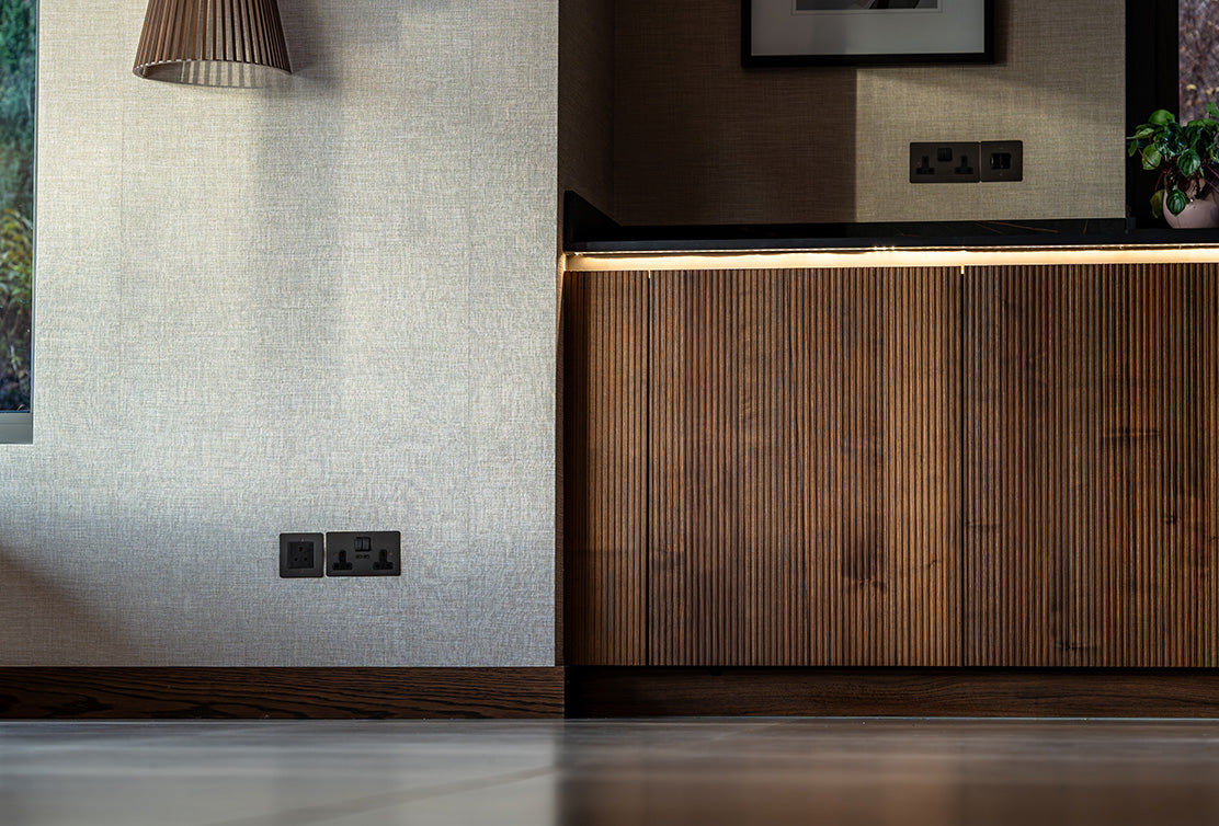 A close-up view of a modern interior with a wooden cabinet, textured wall, and stylish pendant light illuminating the space.