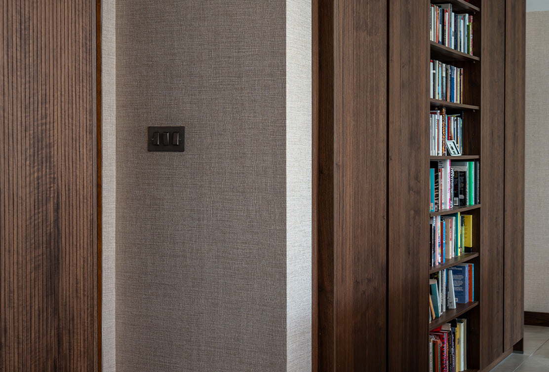 A textured gray wall features a light switch beside a dark wooden bookshelf filled with colorful books in a modern interior.