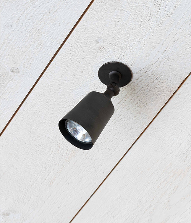 Adjustable bronze 'Perryn Single' surface-mounted spotlight fitted onto a white ceiling plank.
