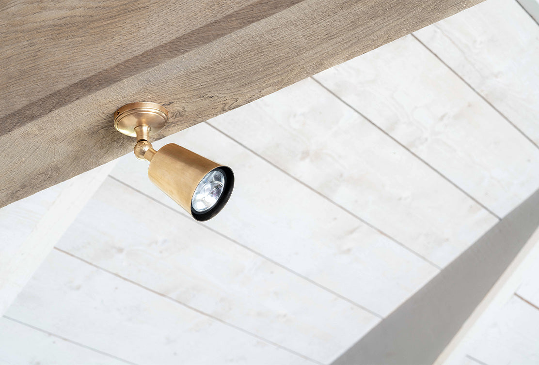 Modifiable 'Baylis Single' spotlight in an antique brass finish, installed neatly on a ceiling beam.