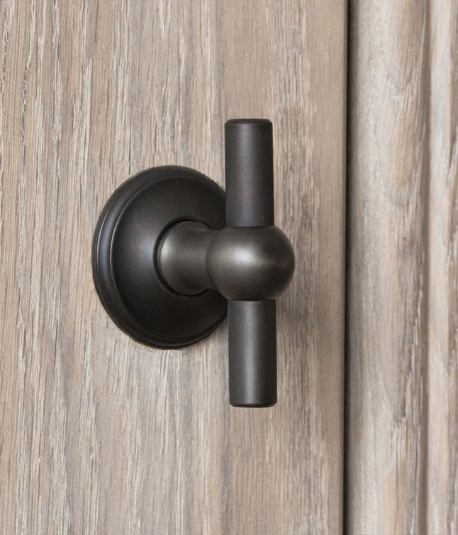 Close-up of a sleek bronze door knob on a wooden door, featuring a modern design with a round base and straight handle.