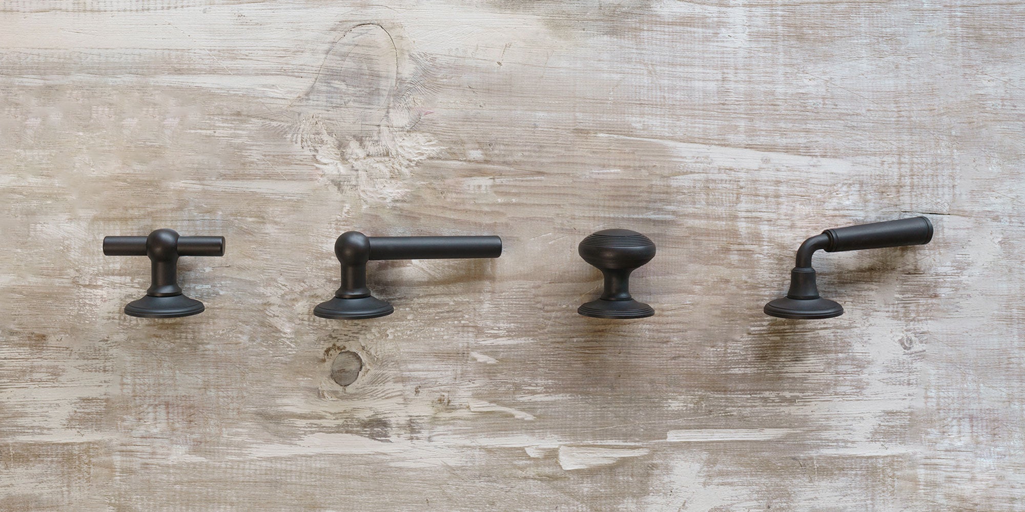 Four stylish bronze cabinet handles displayed against a textured wooden background, showcasing various designs and shapes.