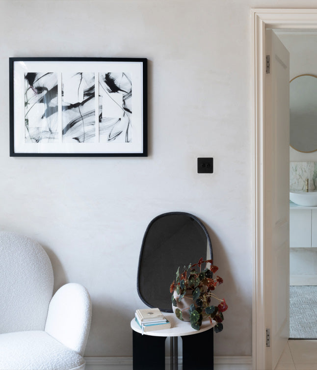 A cozy corner featuring an abstract black and white art piece, a plush white chair, and a stylish side table with a potted plant.