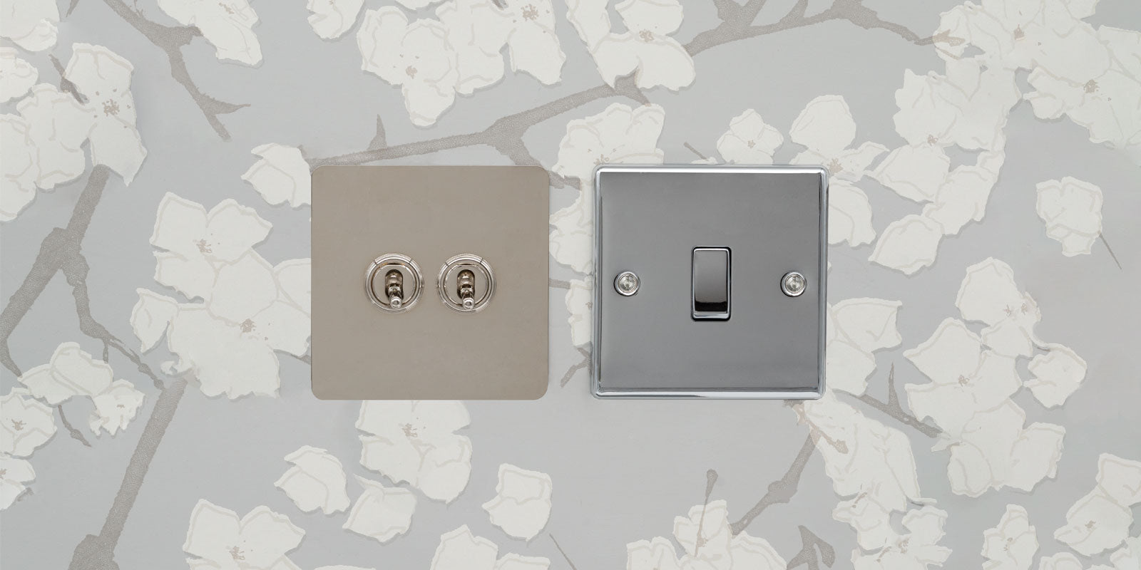A stylish light switch and dual socket set featuring a sleek chrome finish on a floral patterned wall.