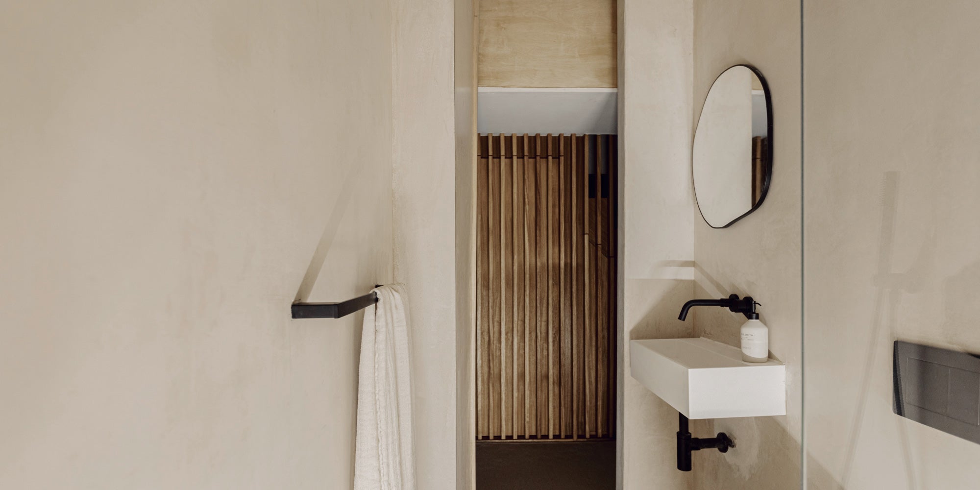 A modern bathroom featuring a white sink, black faucet, round mirror, and a towel on a rack, with wooden paneling in the background. 