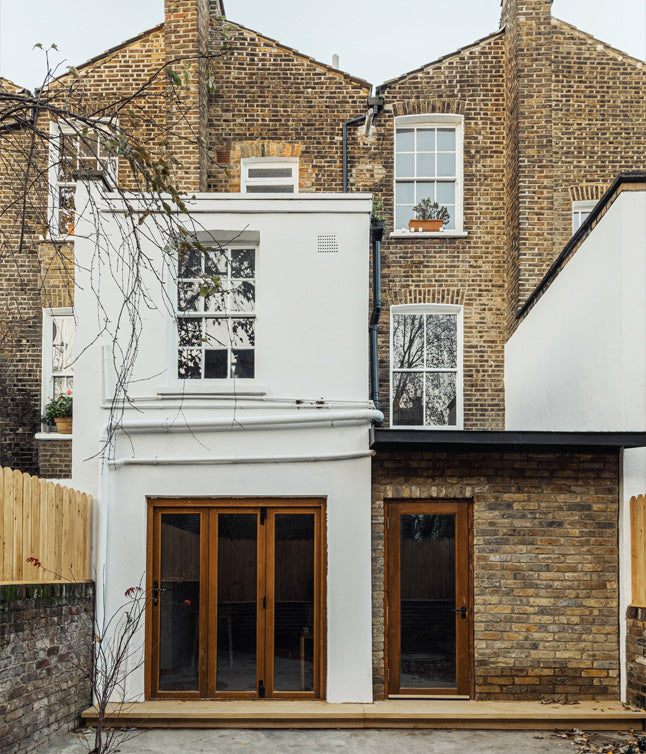 Rear view of a modernized home with a white extension and wooden doors, contrasting against traditional brick walls.