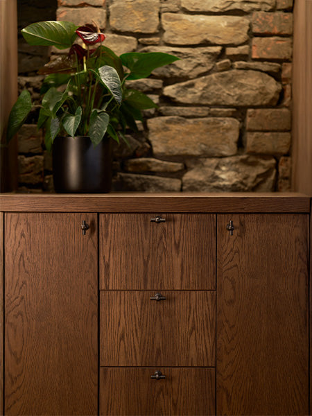 Close-up of a sleek metal door handle on a wooden cabinet, with warm lighting and a blurred wine rack in the background.