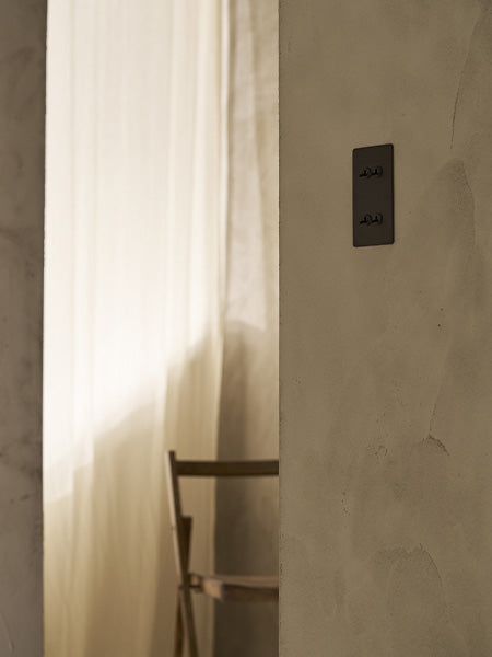 Wooden folding chair and linen curtain, with a bronze '4G Vertical Two Way Toggle Switch' in the foreground.