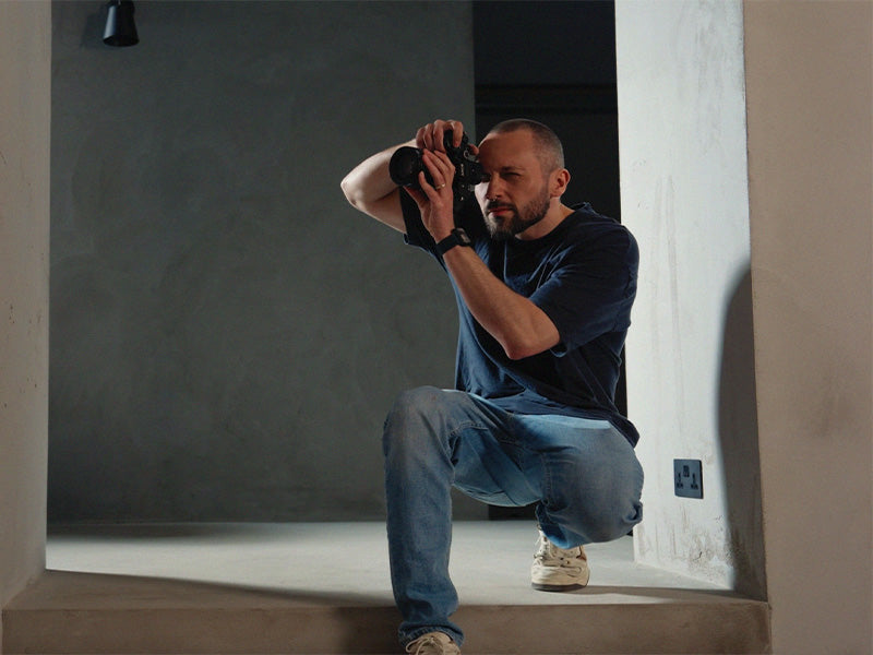 Person crouching to take a photograph in a neutral setting.
