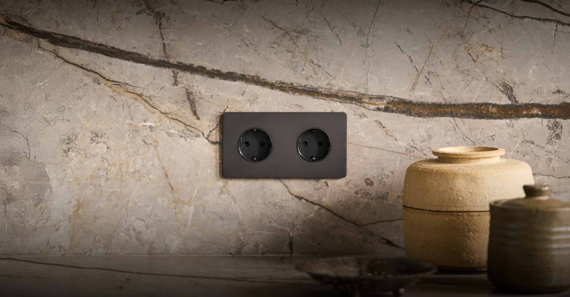 A dark bronze EU socket on a marble wall