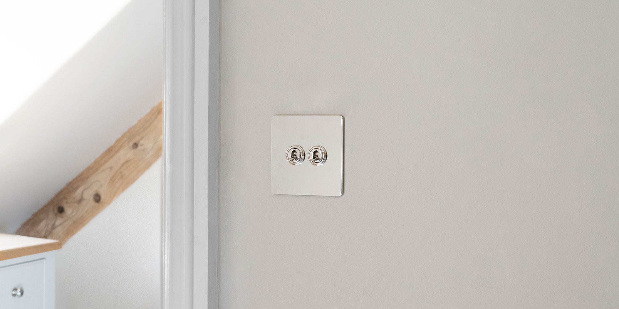 A polished nickel light switch against a soft gray wall, contrasting with natural wood accents in a modern interior setting.