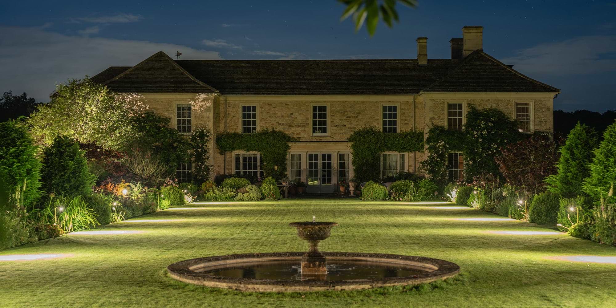 Symmetrically lit garden landscape featuring uniform 'Ealing Path Spotlights' in antique brass.