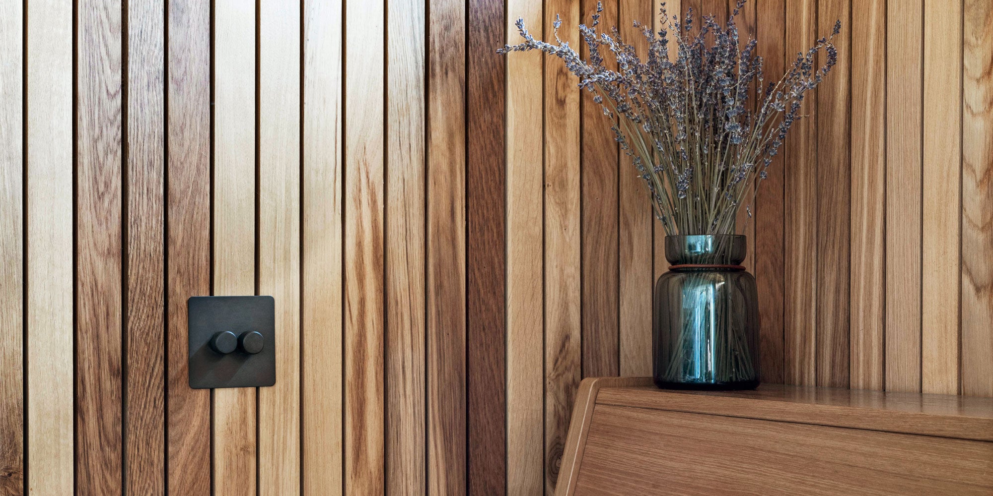 A sleek vase with dried lavender on a wooden shelf, against a backdrop of warm-toned wooden panels. Text overlay features Lee Thornley from Bert & May.