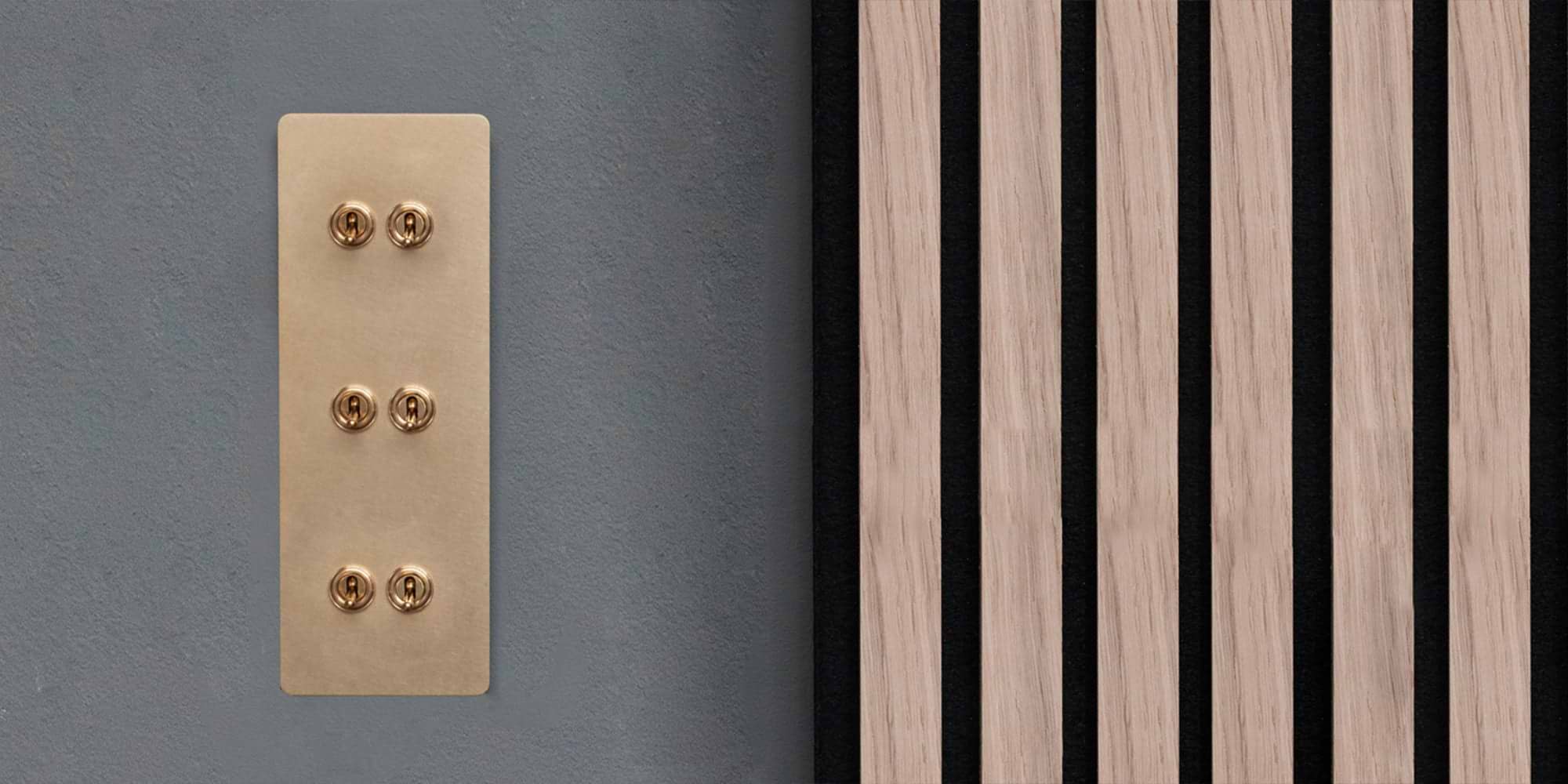 A brass panel with six toggles is mounted on a gray wall, beside vertical wooden slats alternating with black accents.