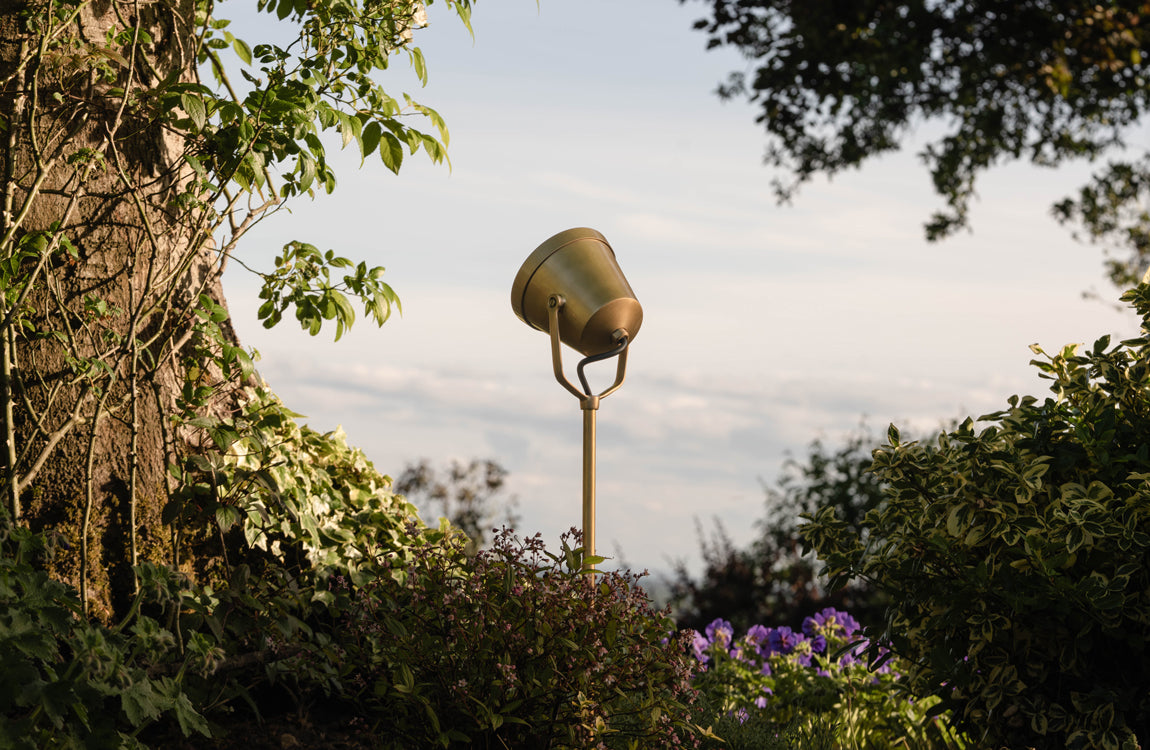 Outdoor 'Ealing Ground Spotlight' casting a warm glow on an orange wall, surrounded by pebbles on the ground.