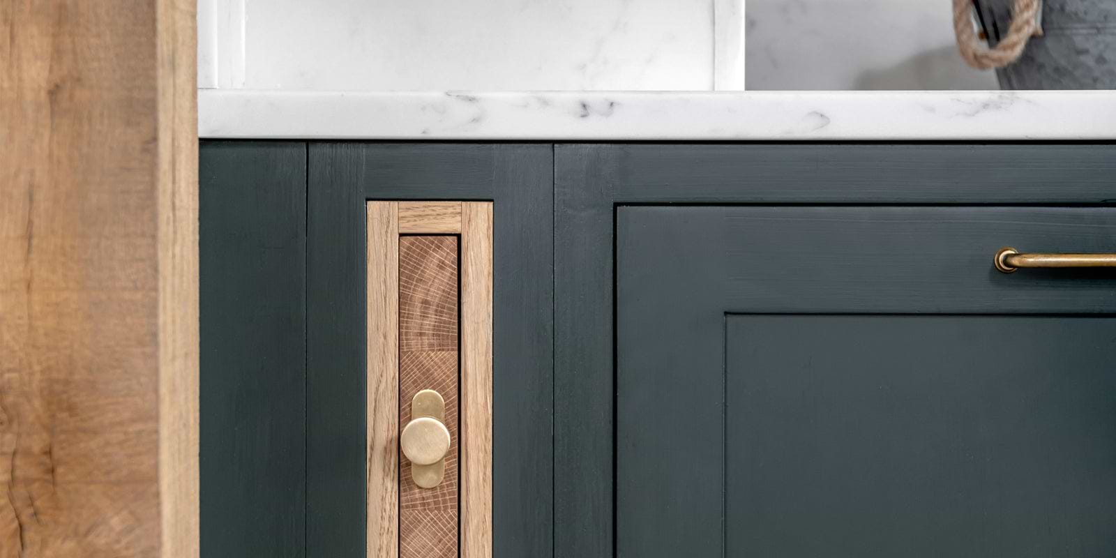 Close-up of modern cabinetry featuring dark green paint, natural wood accents, and a circular brass knob for a sleek, contemporary look.