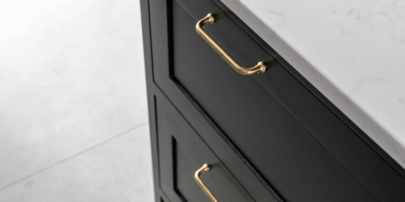 Close-up of black kitchen cabinet drawers featuring elegant gold handles, set against a light marble countertop.