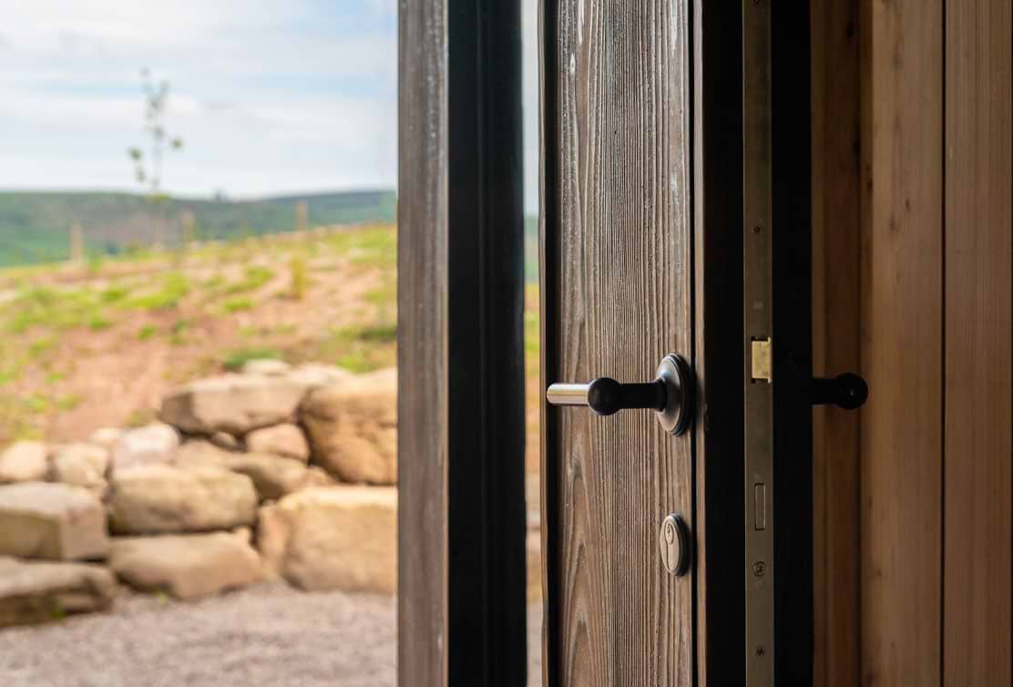 A close-up of an open wooden door featuring a sleek black handle, revealing a lush outdoor landscape beyond.