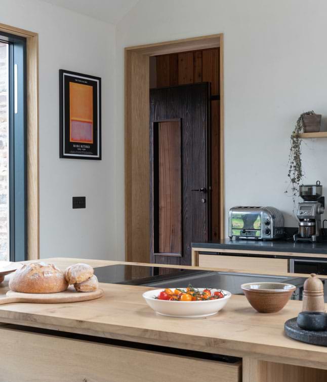 A modern kitchen features wooden countertops, fresh tomatoes in a bowl, bread on a plate, and a sleek toaster.