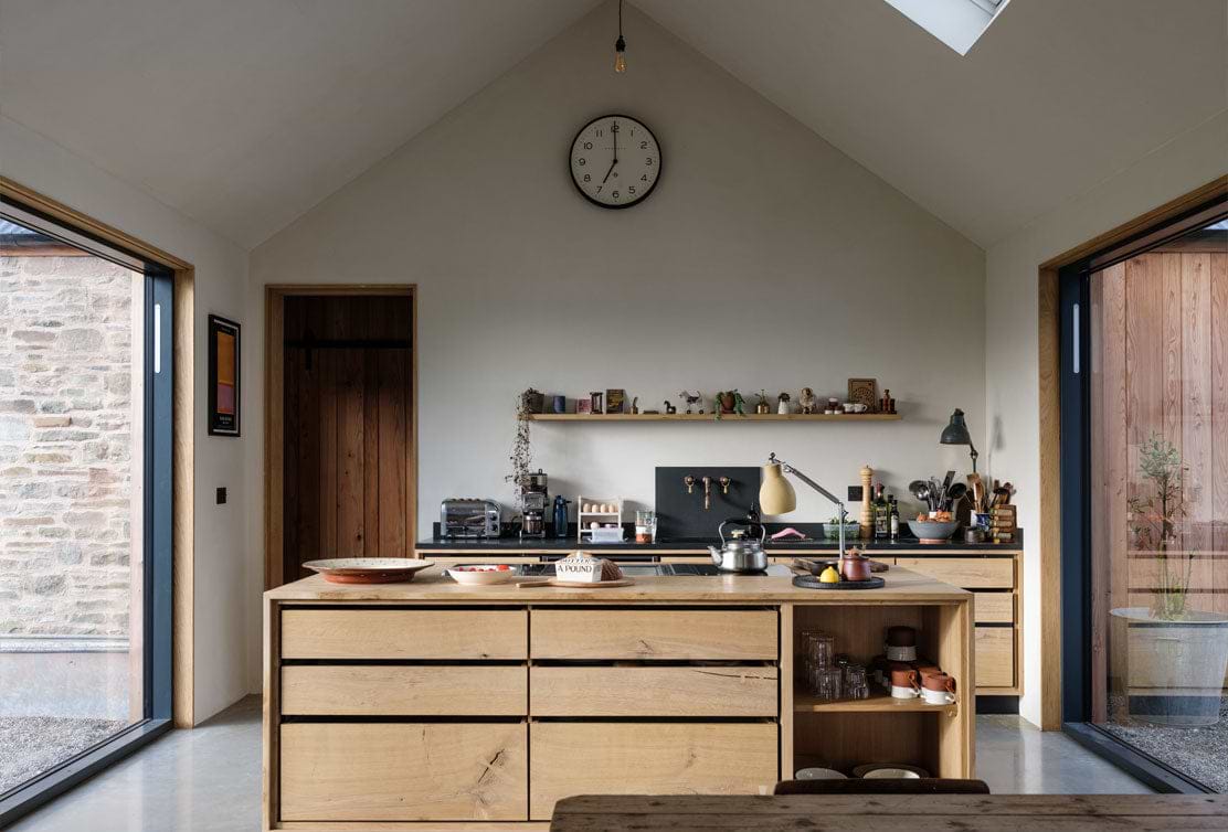 Modern kitchen with wooden cabinets, open shelving, and large windows, featuring minimalistic decor and natural lighting.