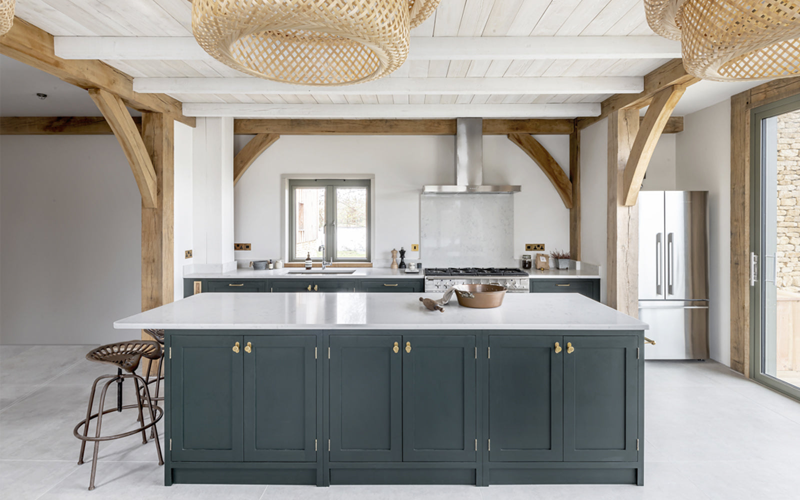 Modern kitchen with dark green cabinetry, white marble countertop, wooden beams, and stylish pendant lights.