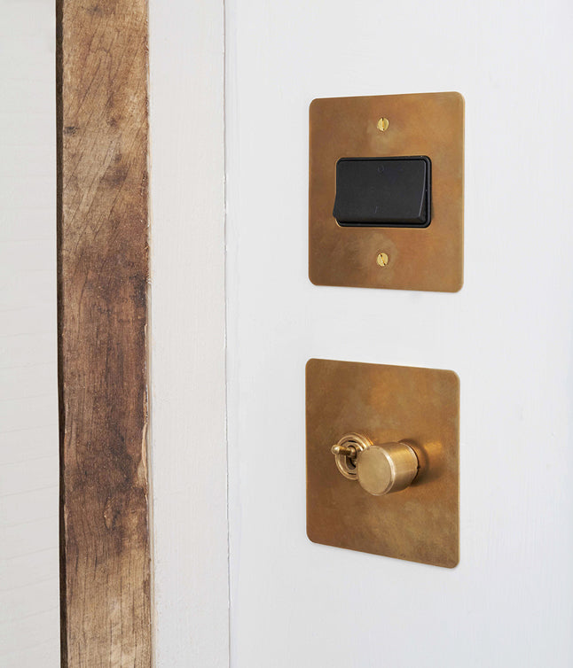 Close-up of a white door with a brass light switch and a round brass door lock, adjacent to natural wood trim.