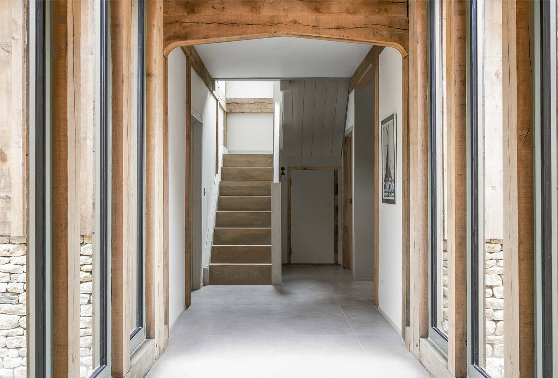 Bright hallway featuring wooden accents, large windows, and a staircase leading to the upper floor, creating a modern rustic aesthetic.
