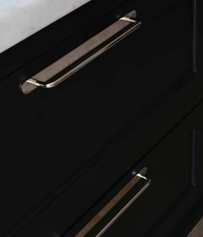 A close-up view of sleek silver drawer handles against a matte black cabinet with a marble countertop above.