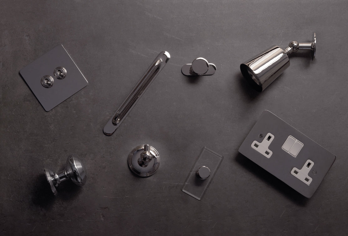 A collection of modern chrome hardware pieces, including switches, knobs, and a light fixture, set against a dark surface.