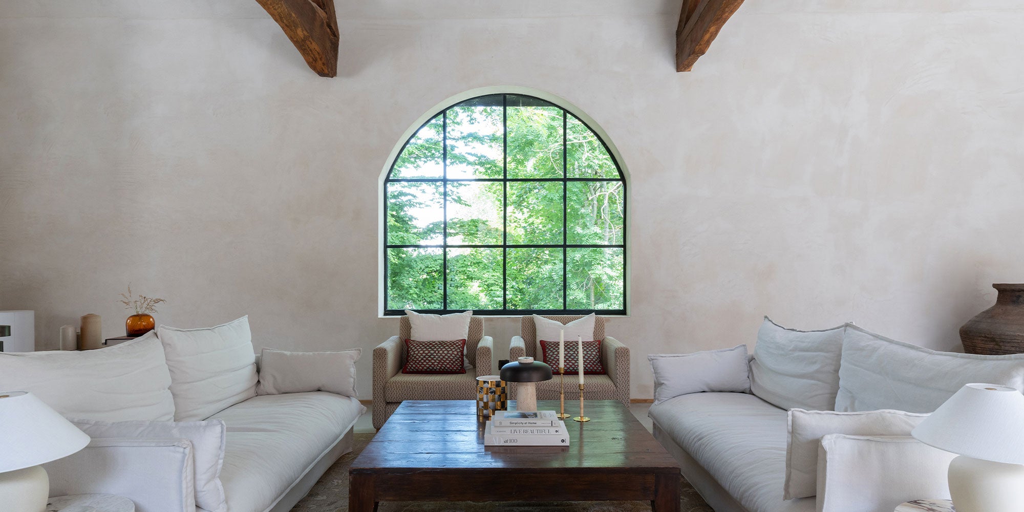 A bright, airy living room with a large arched window, featuring a cozy couch, decorative pillows, and a wooden coffee table.