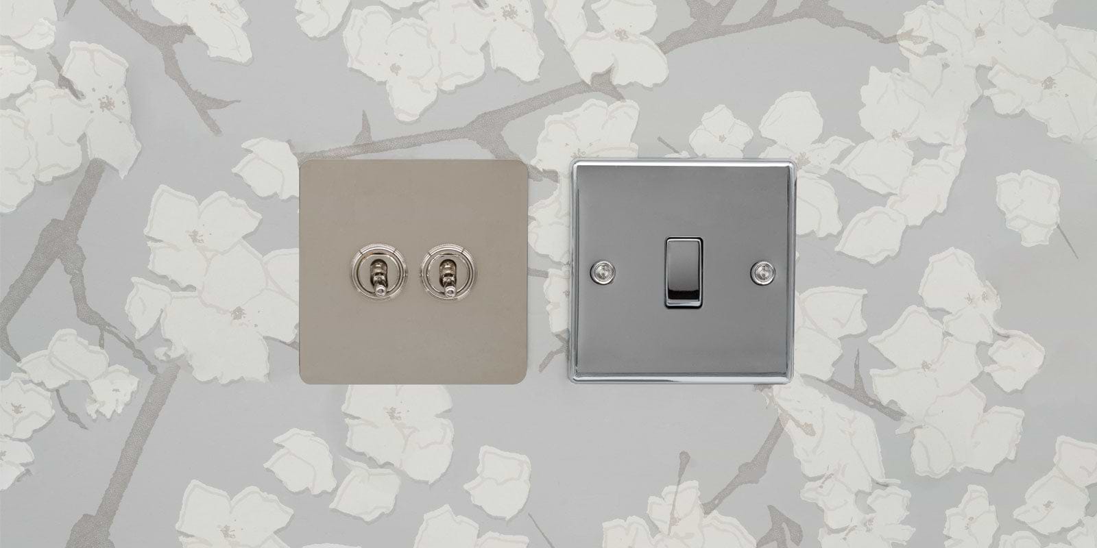 A stylish light switch and dual socket set featuring a sleek chrome finish on a floral patterned wall.