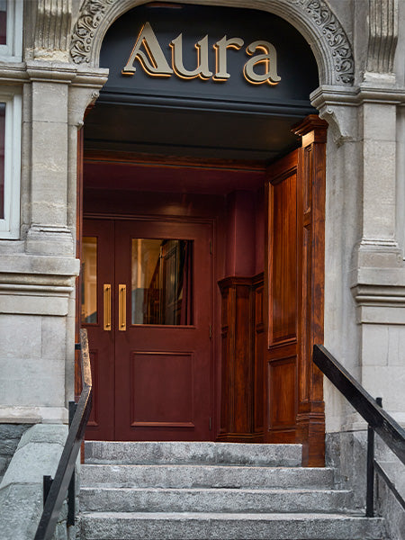 Entrance to Aura with elegant dark wood accents and maroon doors, inviting guests into a stylish establishment.