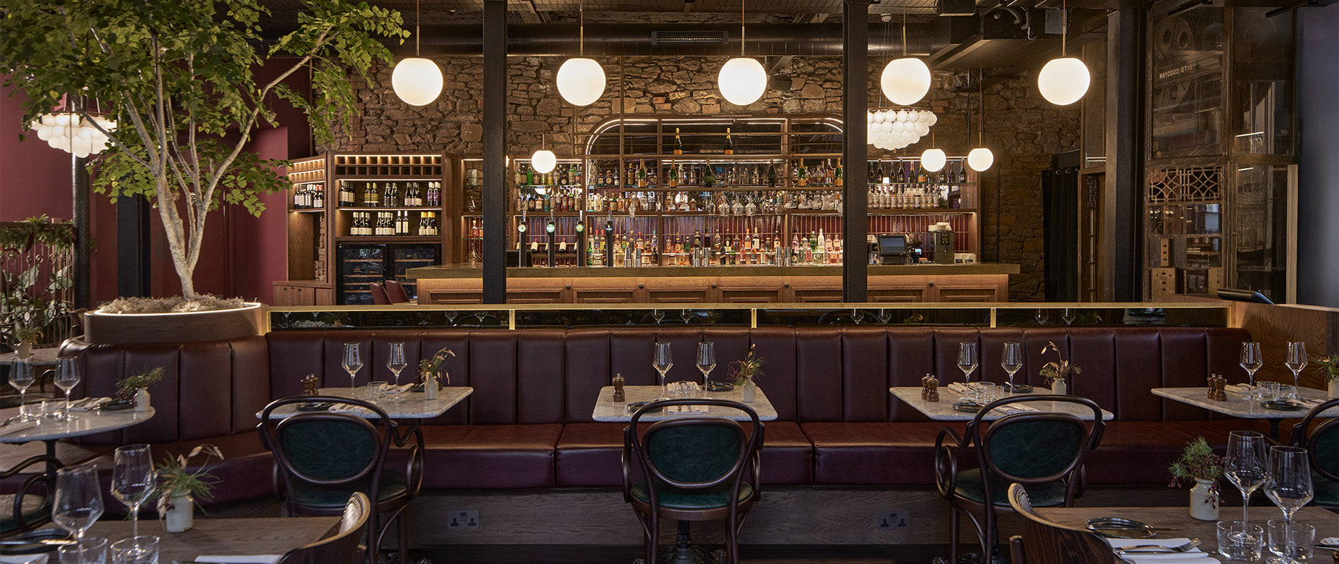 Elegant restaurant interior featuring a stone wall, stylish bar, plush seating, and ambient lighting with greenery accents.